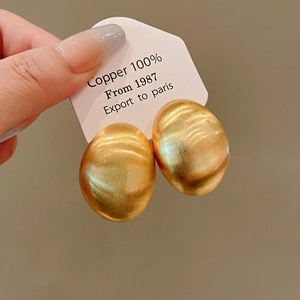 Primo piano di eleganti orecchini ovali in oro spazzolato su una carta bianca da esposizione.
