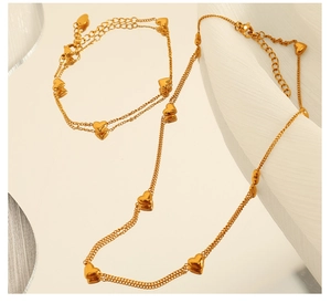 Detail view of gold heart necklace and bracelet set with layered chain on a wavy texture