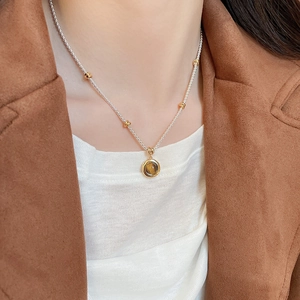 Detail shot of tiger eye stone pendant on a silver and gold beaded necklace worn on neck