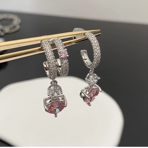 Détail macro d'une boucle d'oreille argentée avec cœur rose et pierres en zircon
