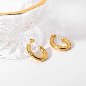 Détail de boucles d'oreilles ovales dorées en forme de C sur fond blanc avec décor