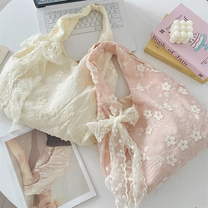 Detail of embroidered floral tote bags with lace bow handles in cream and pink