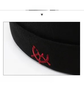 Detail view of red rudder embroidery on black knitted brimless dockercap fabric