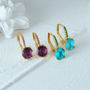 Detailed macro view of gold earrings with sparkling purple and teal crystals on white