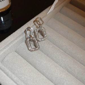 Macro detail of geometric silver earrings with small crystals on a grey velvet tray