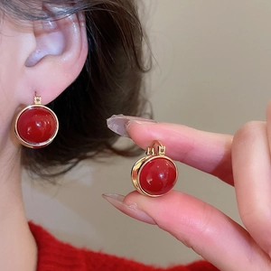 Detail view of round red and gold earrings featuring a polished red gem and metallic finish