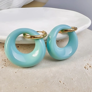 Close-up of light blue resin oval earrings with 18K gold plated hoops on a stone tray