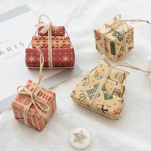 Mini Christmas gift box ornaments with red snowflake patterns and twine on white plush rug