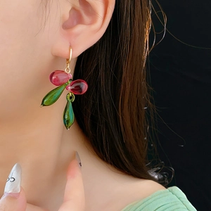 Détail de boucles d'oreilles feuille rose et fruit vert sur mannequin au fini brillant