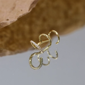 Detail of a triple-layer gold ear cuff with marquise zircons on a reflective mirror