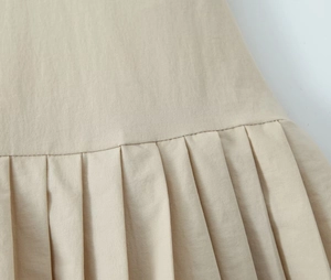 Nahaufnahme der plissierten Textur eines beigen Mini-Kleides im Sweet-and-Spicy-Stil