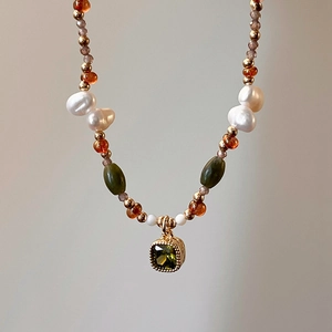 Detailed macro view of 18k gold vintage necklace with baroque pearls and green gemstones