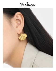 Gros plan de boucles d'oreilles feuille de ginkgo dorées avec texture métal brossé