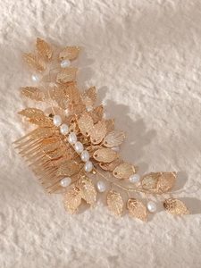 Macro detail of bridal hair comb with golden leaves and white pearls on textured paper