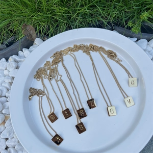 Detailed view of gold square letter pendants on fine chains over white pebbles