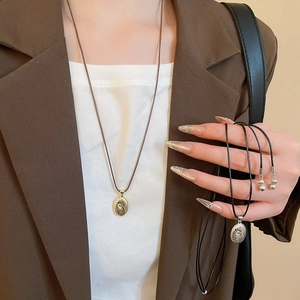 Close-up of gold and silver spiral oval pendants on wax cords worn by a model