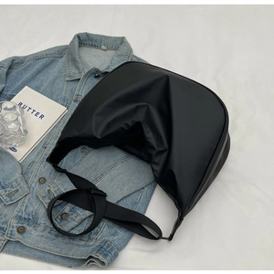 Detail of minimalist black crossbody bag on white fabric with blue denim and magazine
