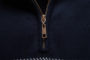 Dettaglio macro della cerniera in metallo bronzo e trama in maglia blu scuro del maglione uomo