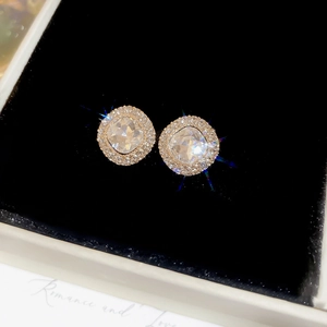 Macro shot of sparkling round zircon stud earrings set in gold metal on black velvet box