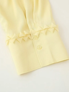 Close-up of pale yellow chiffon sleeve with button cuffs and ruffled pleat detail
