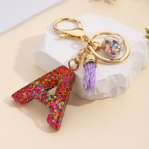 Detail of resin letter A keychain with colorful sequins, purple tassel, and gold metal clasp