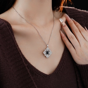 Close-up of silver necklace with cross flower pendant featuring a blue gemstone