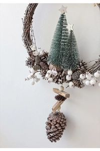 Detail showing natural pine cones and small frosted Christmas trees on a vine wreath