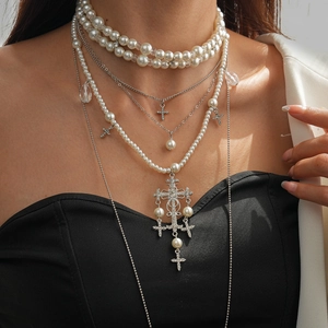 Close-up of layered faux pearl and silver cross pendant necklace on a female model