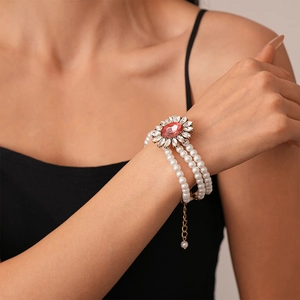 Detail of triple-layer pearl bracelet with pink gemstone flower charm on a model's wrist