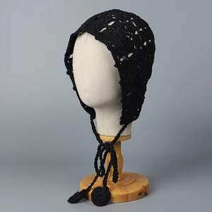 Vue détaillée d'un bonnet en crochet noir fait main avec motifs ajourés et pompons longs