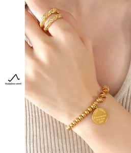 Detail of gold beaded bracelet with engraved round pendant and matching textured ring