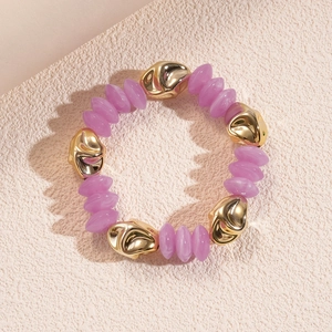 Detail of purple acrylic beads and irregular gold metal pieces on a textured beige surface