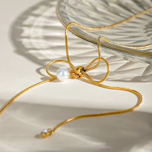 Macro detail of 18k gold plated bow pendant necklace with pearl on glass tray