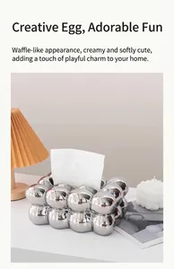 Silver marshmallow tissue box next to a pleated lamp and candle in a cozy home setting