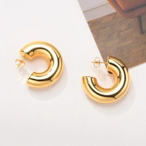 Detail of high-polish C-shaped gold-plated stainless steel earrings with ball pins