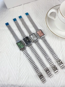 Variety of ladies square quartz watches with colorful dials on white fabric background