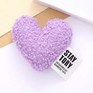 Detail of a purple plush heart accessory with a fabric label on a white background