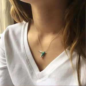 Close-up of a blue-green gradient hummingbird pendant necklace on a gold chain