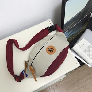 Close-up of beige and burgundy canvas bag featuring leather logo and zip puller details