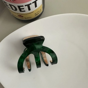 Close-up of a dark green tortoiseshell hair claw clip with golden top accent on a plate