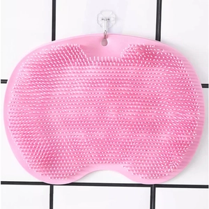 Pink silicone back scrubber and foot massage mat hanging on a tiled bathroom wall