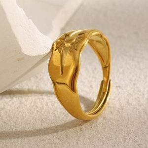 Close-up of gold starburst engraved adjustable ring on white stone and sand texture