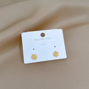 Minimalist gold snowflake stud earrings on display card with luxury silk background