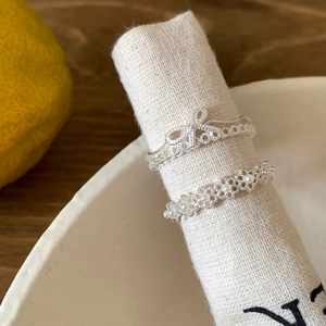 Elegant silver-toned bow and pearl floral open rings shown on a rustic linen display