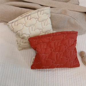 Close-up of quilted cosmetic bags in red and cream with cute rabbit embroidery patterns