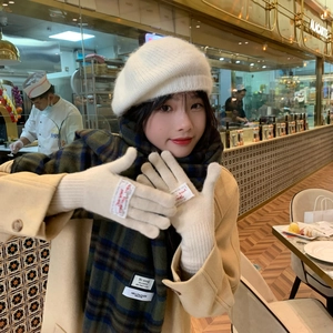 Matching set of white knit beret, beige gloves, and green plaid scarf in a cozy cafe