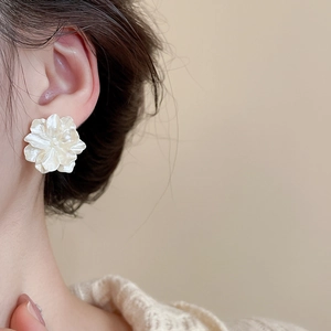 Detailed view of elegant white flower pearl earrings worn on a model with soft lighting