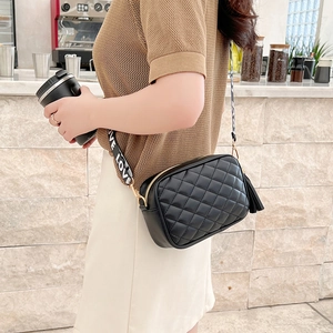 Quilted black crossbody bag with LOVE strap and tassel shown in a cafe setting