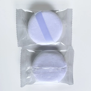 Detailed view of two round white crystal velvet powder puffs in clear packaging with purple ribbon