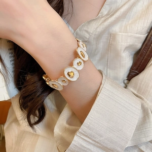 Close-up of gold irregular enamel stretch bracelet on wrist with cream texture background